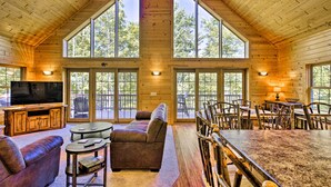 A spacious lodge with a high ceiling, large windows, a cozy seating area, and a dining setup. - Lakefront Wisconsin Cabin with Boat Dock! (Birchwood)