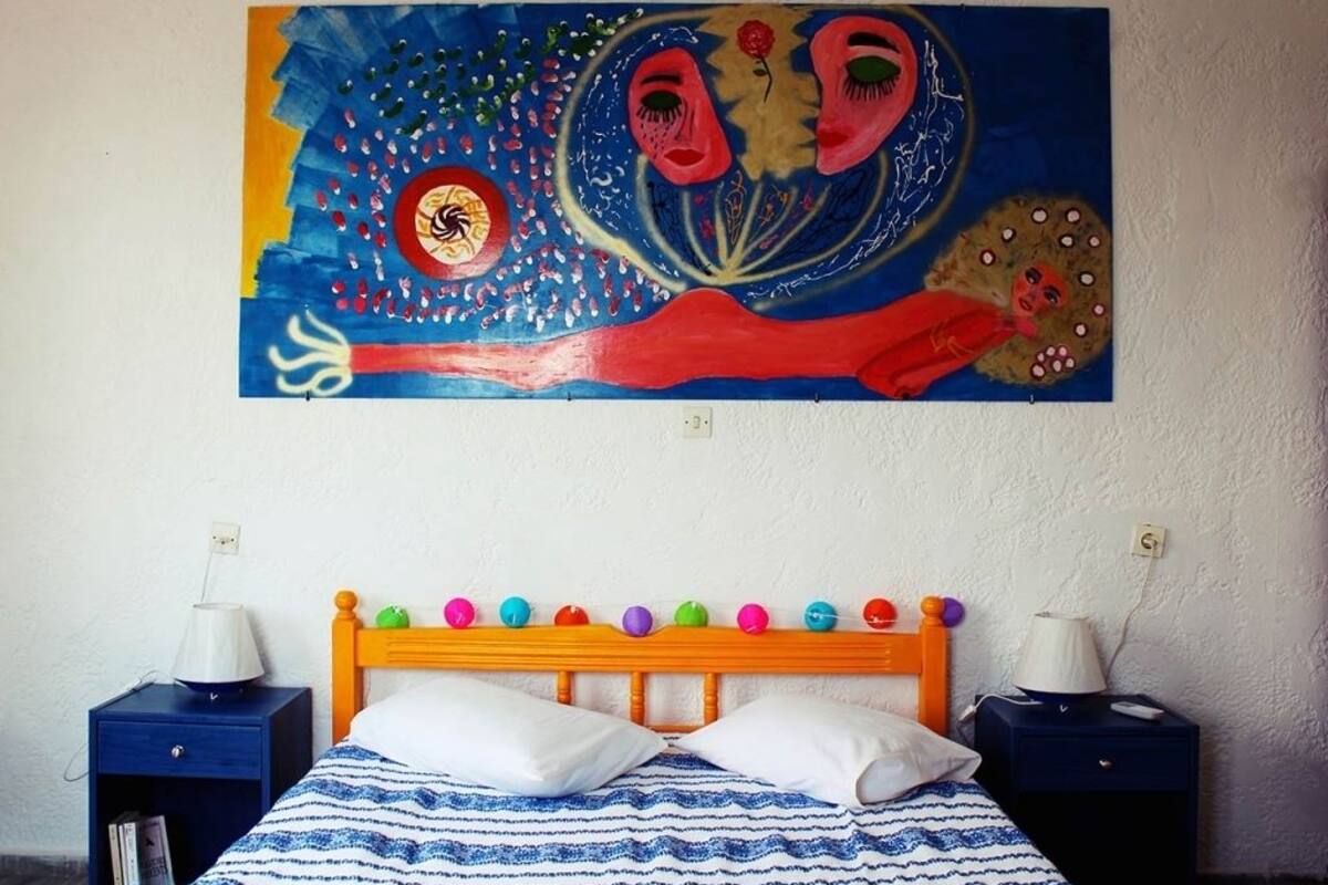 A bedroom with a bed, two bedside tables, a colorful painting, and a wooden headboard with decorative balls.
