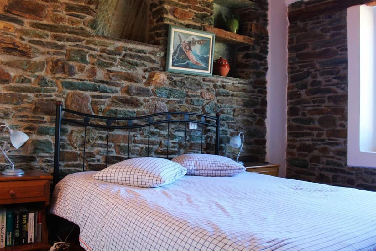 A bedroom with a stone wall, a metal bed frame, a bedside table with a lamp, and a framed picture above the bed.
