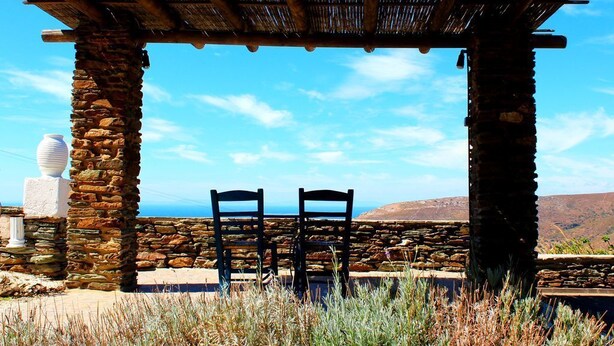 A stone structure with two chairs under a thatched roof, overlooking a scenic landscape. - Villette Adonis (Andros)