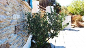 A stone wall adjacent to a wooden deck with a small tree. - Villette Adonis (Andros)