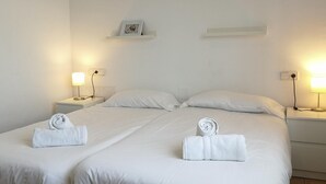 Et hotelværelse med to senge, hvide sengetøj og to sengeborde med lamper.