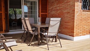 En udendørs terrasse med bord og stole, en glasdør ind til et indre rum, samt en murstensvæg.