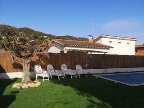 A backyard with a swimming pool, white lounge chairs, a tree, and a bamboo fence. - ROSERS - House with private pool, barbecue 20 minutes Barcelona (Cabrils)
