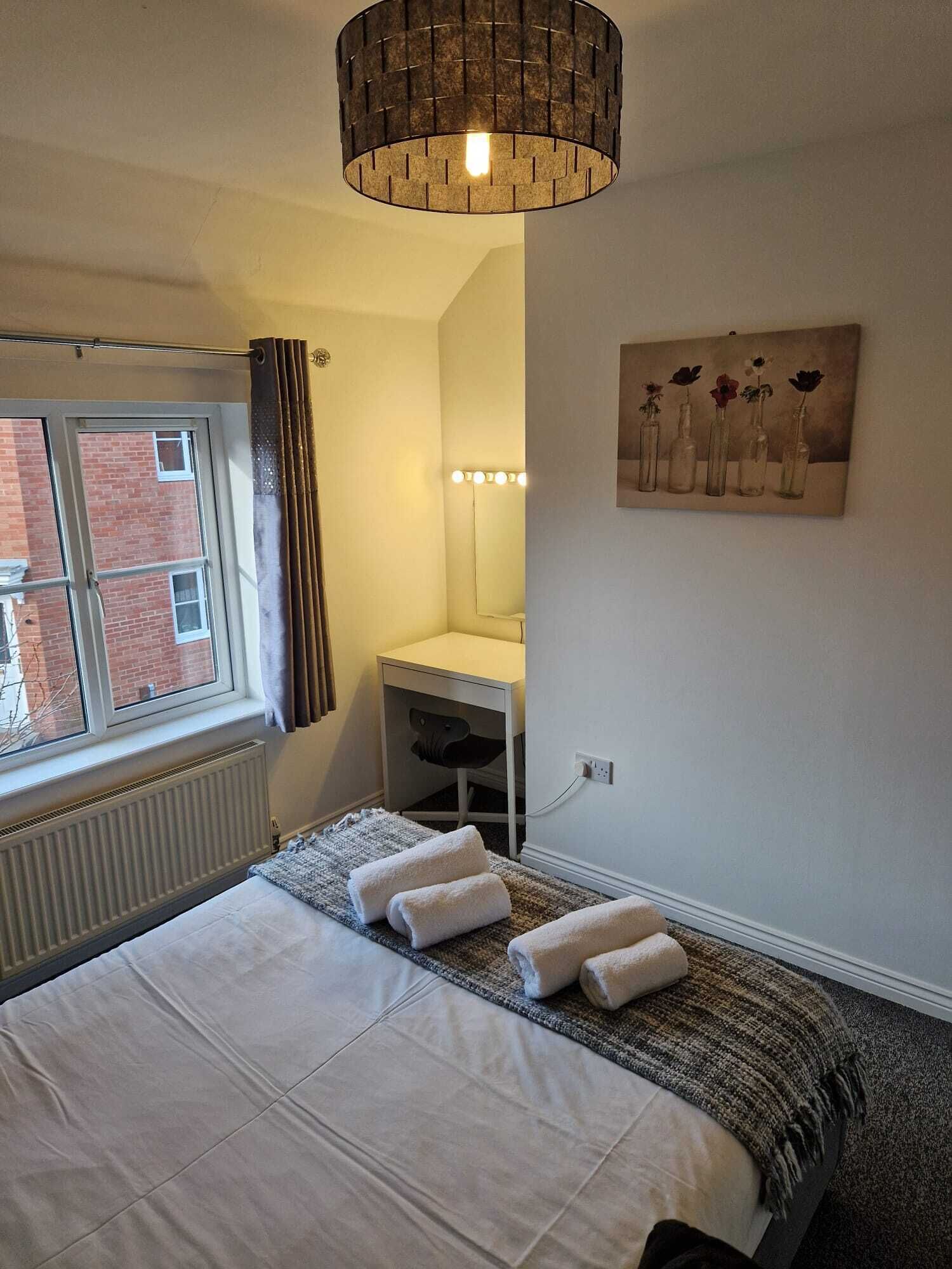 Une chambre à coucher avec un lit, une table de chevet, un miroir et une fenêtre avec des rideaux.