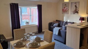 A dining area with a table set for four, a sofa, and a small kitchen area with a counter. - Mayflower Coach House (Hereford)