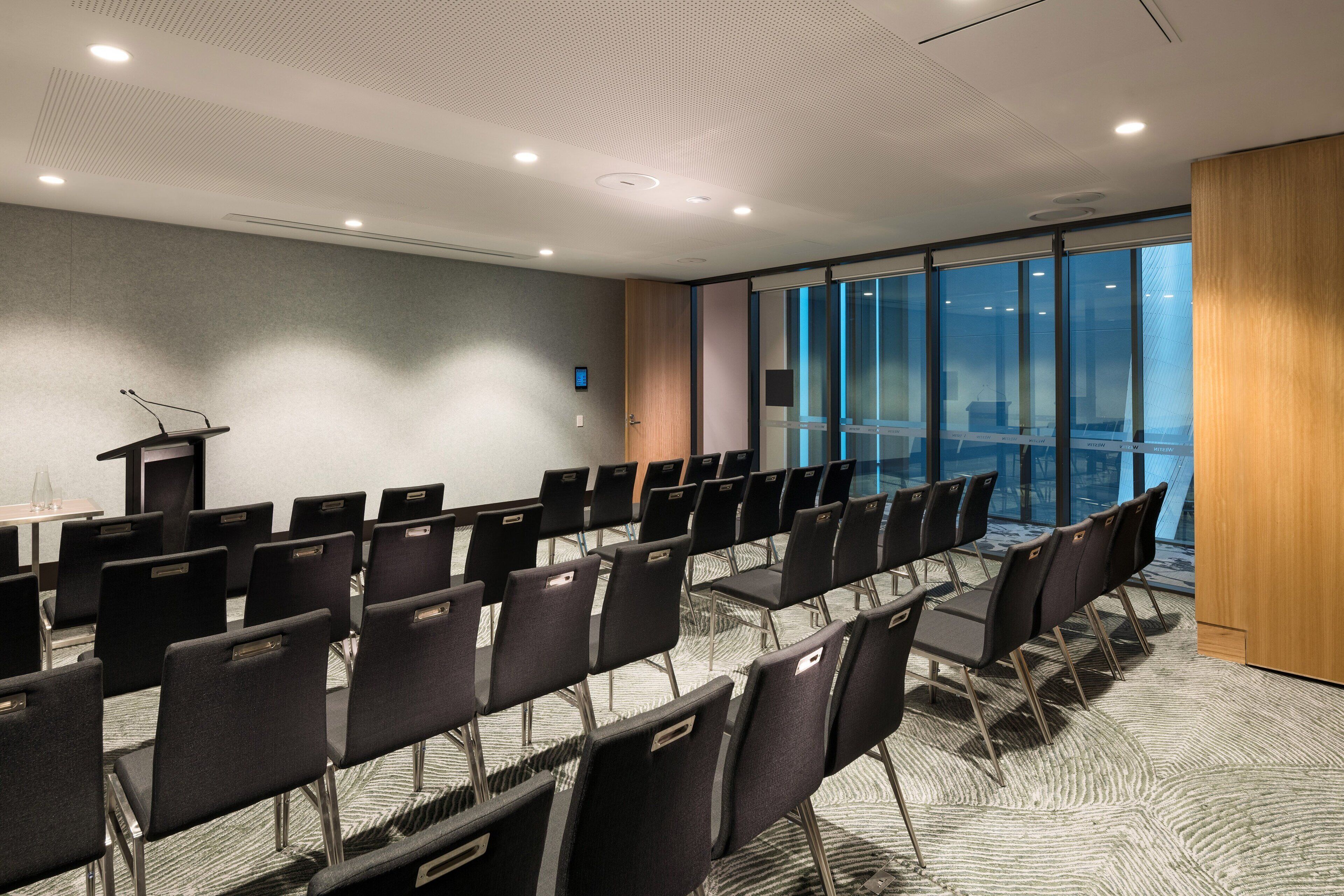 Un salón de conferencias con hileras de sillas, un atril y un ventanal con vistas.
