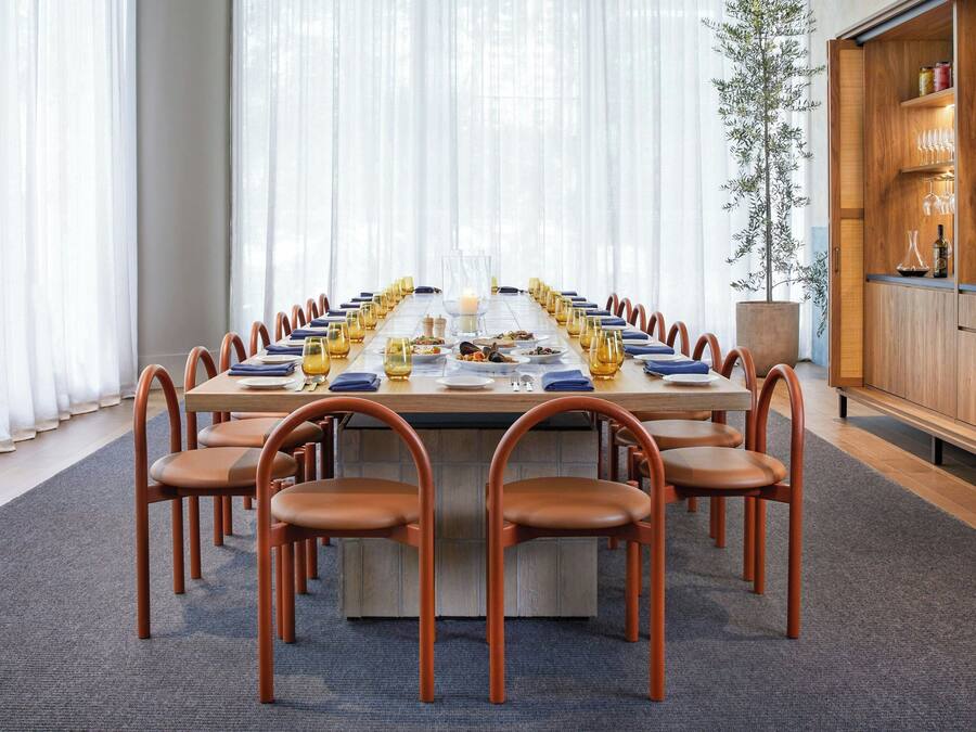A long rectangular table with chairs, a glass centerpiece, and a potted plant.