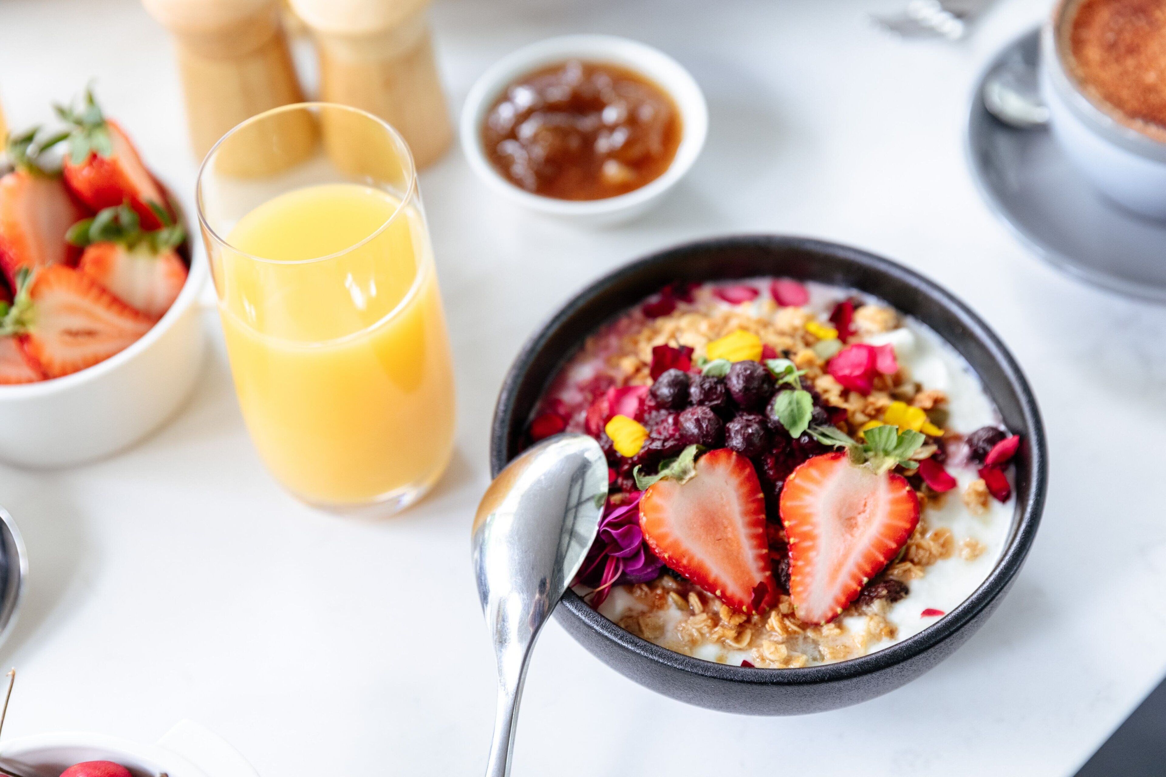 A breakfast setting with a bowl of cereal topped with fruits and a glass of orange juice.