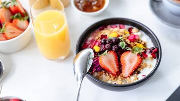 A breakfast setting with a bowl of cereal topped with fruits and a glass of orange juice.