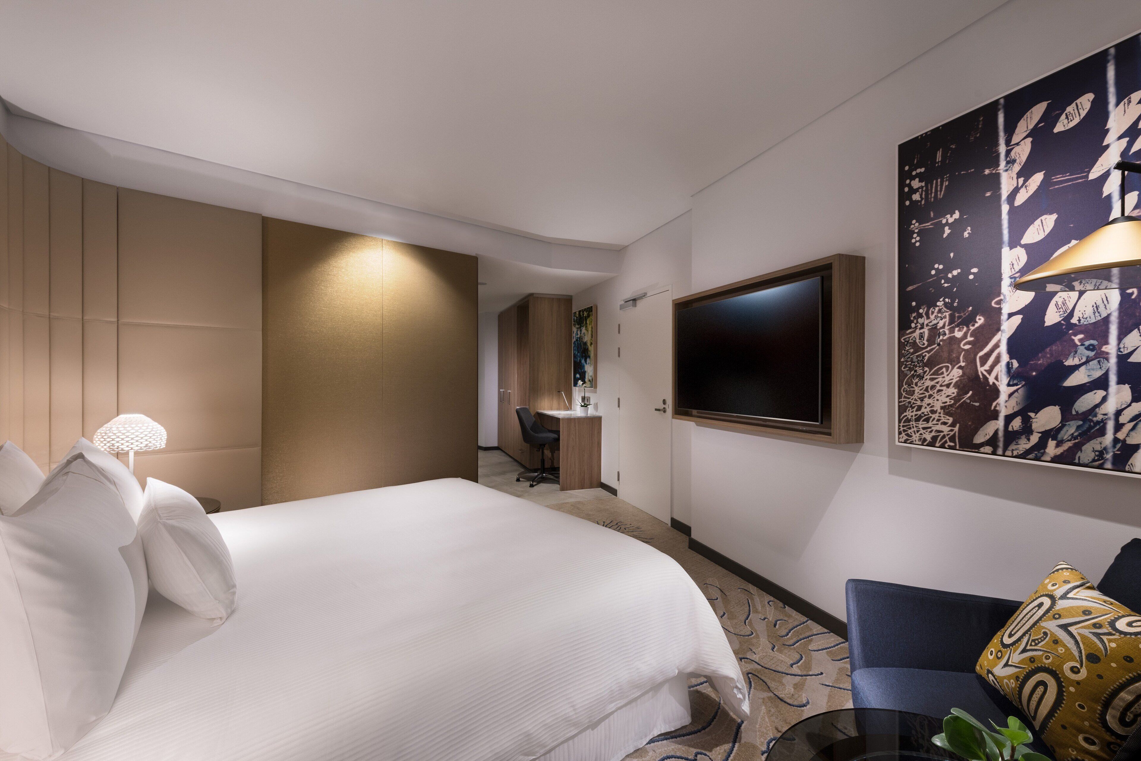 A modern hotel room with a large bed, a desk, and a TV.