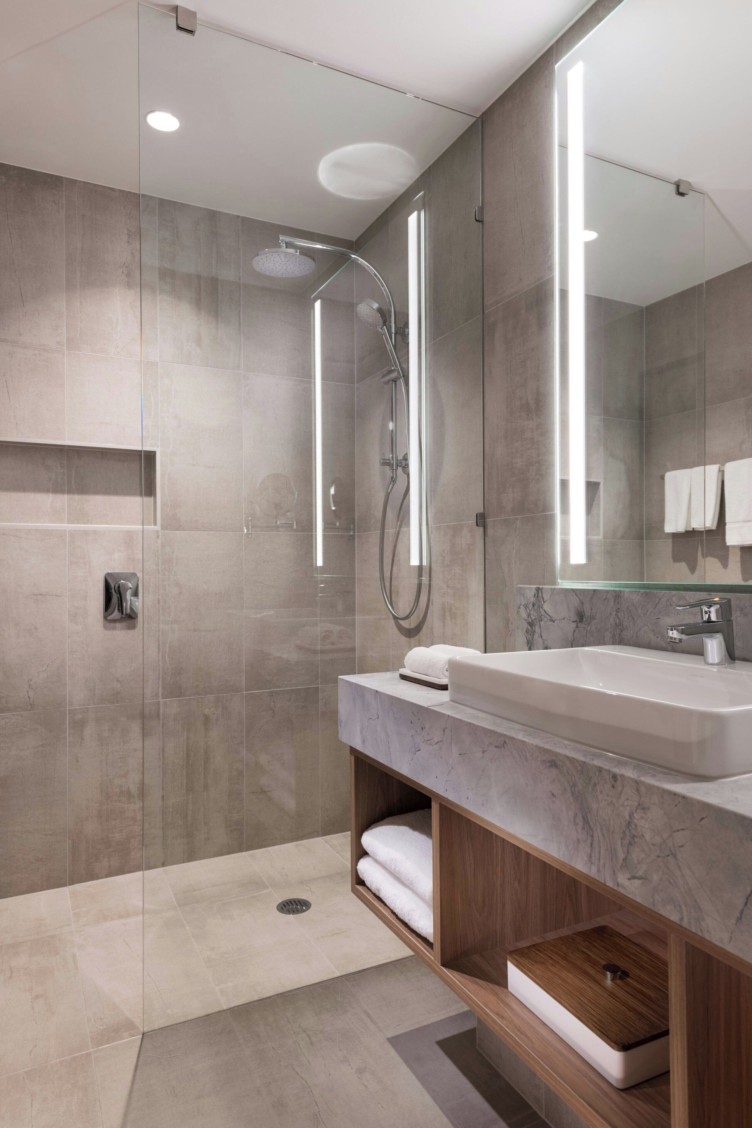A modern bathroom with a large mirror, a shower, and a vanity with a sink and towel storage.