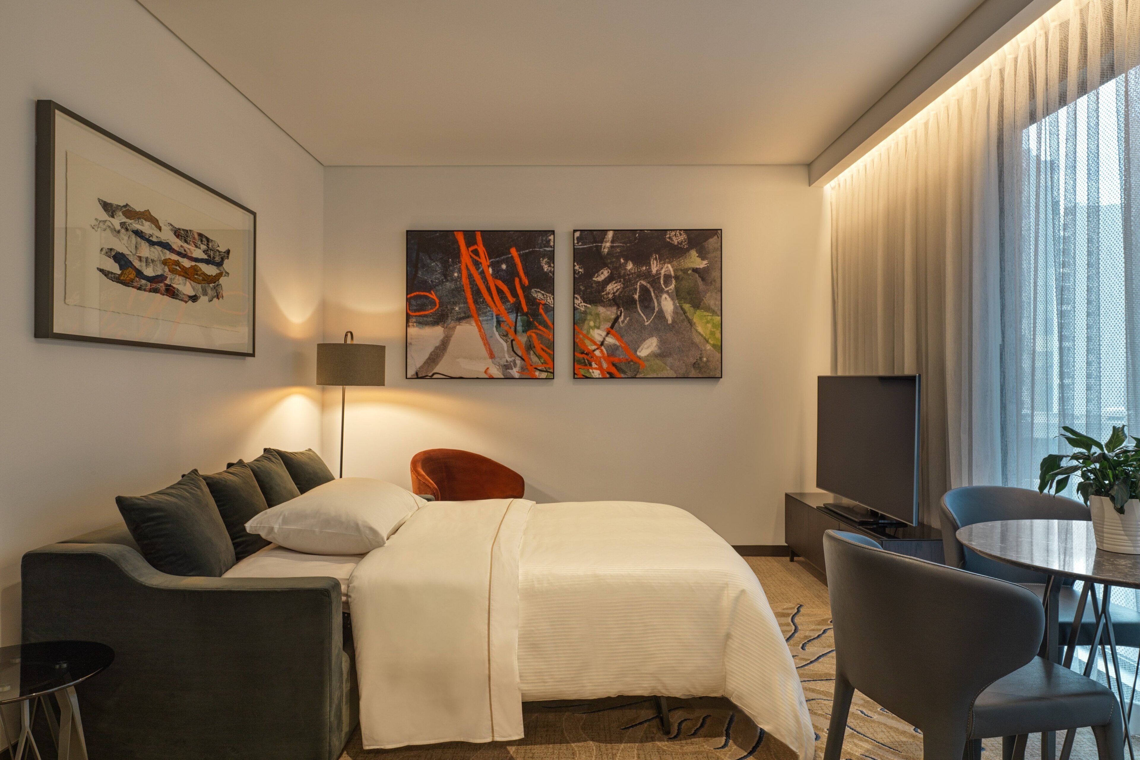 Una habitación de hotel moderna con una cama, un escritorio, una silla y dos obras de arte en la pared.