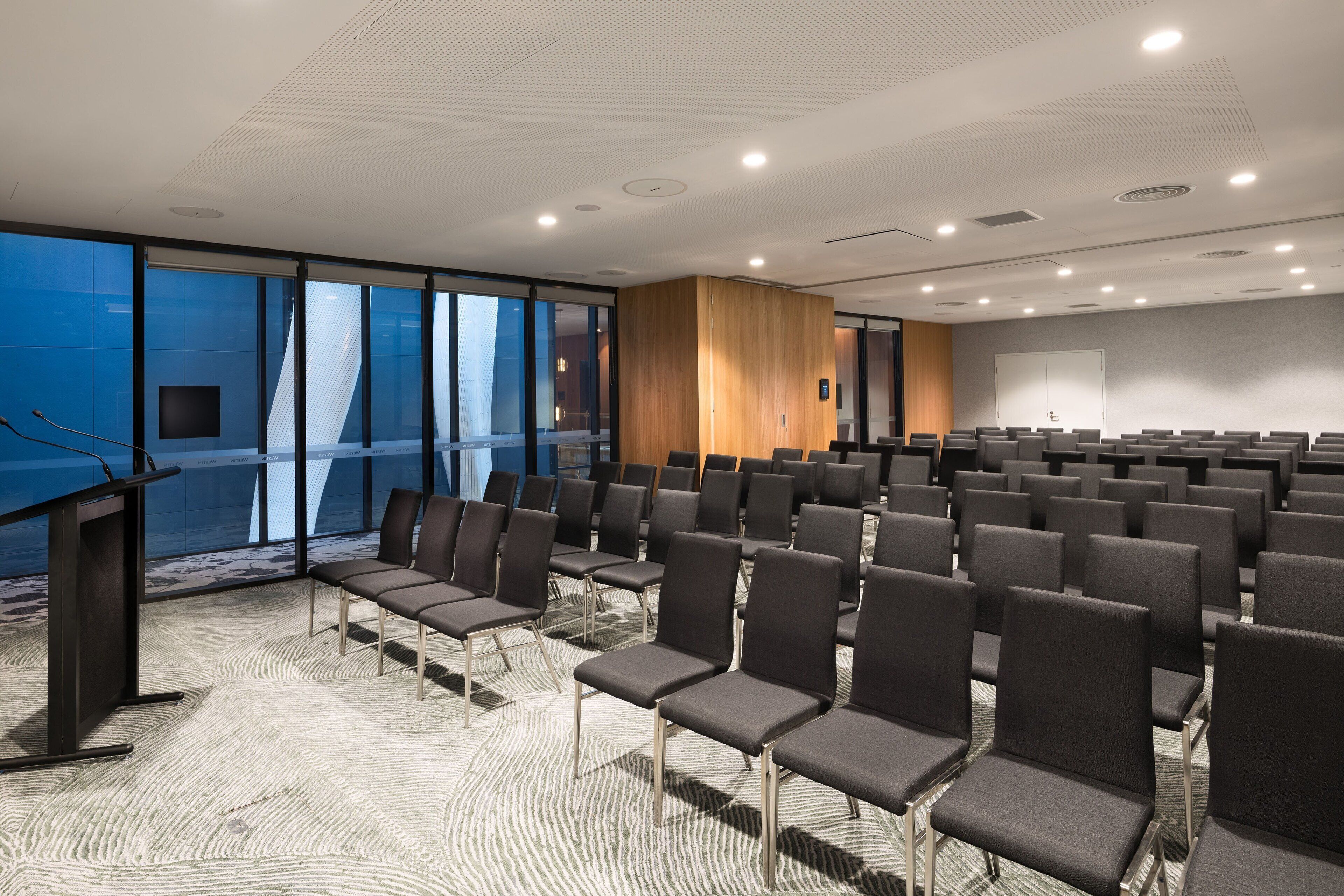 A conference room with rows of chairs, a podium, and large windows offering a view.