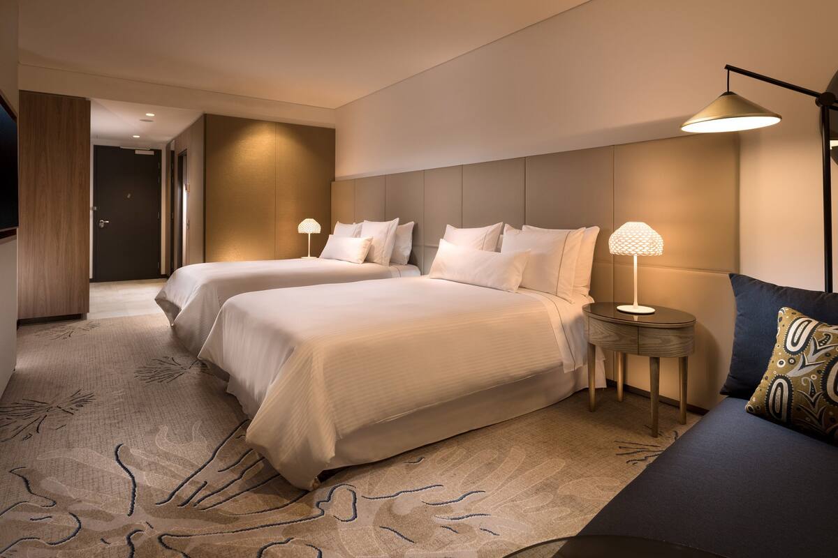 A hotel room with two beds, a sofa, a lamp, and a patterned rug.