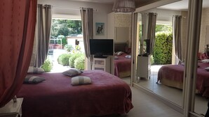 Une chambre d’hôtel avec deux lits, une télévision et un grand miroir qui reflète la pièce et offre une vue sur le jardin.