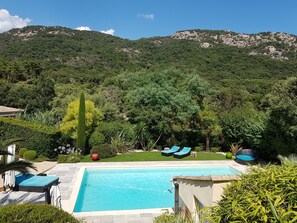 A swimming pool with lounge chairs and a view of a mountainous landscape.
