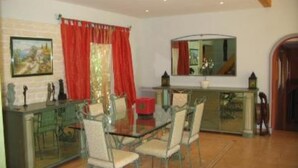Un coin repas avec une table en verre, quatre chaises, un rideau rouge et un tableau accroché au mur.