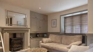A living room with a fireplace, a sofa, a coffee table, and a window with blinds. - Linnet House, Shropshire (Ludlow)