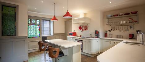 A modern kitchen with white cabinetry, a central island, red pendant lights, and a breakfast bar.
