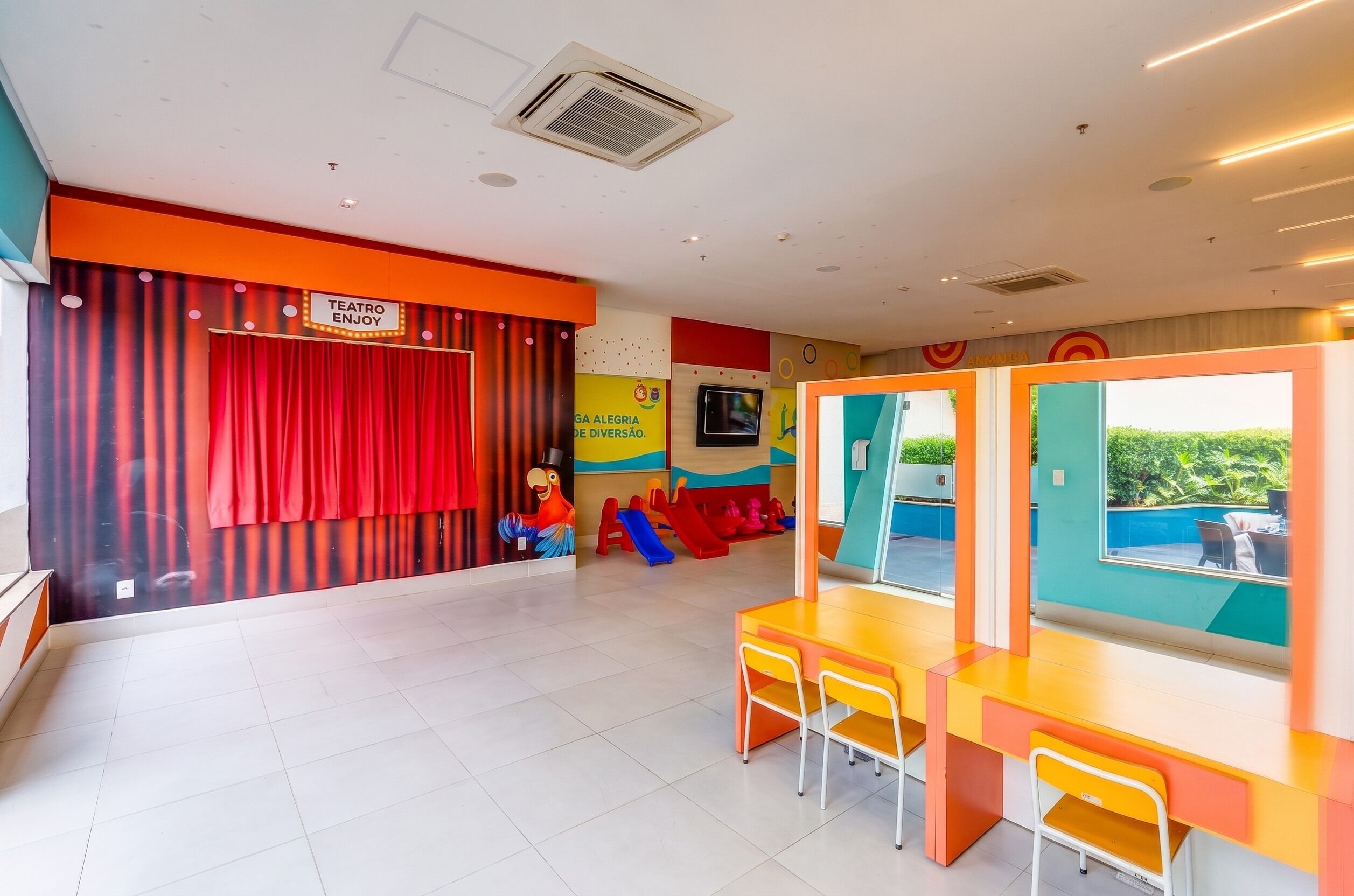 A children's play area with a red curtain backdrop, colorful play structures, and a seating area with a view.