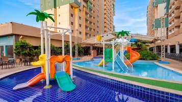 Una piscina con toboganes, una zona de juegos acuáticos y un edificio al fondo.