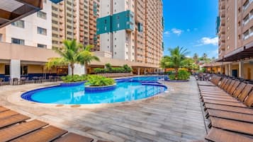 Zona de piscina de hotel con sillas de descanso, una piscina y edificios altos al fondo.