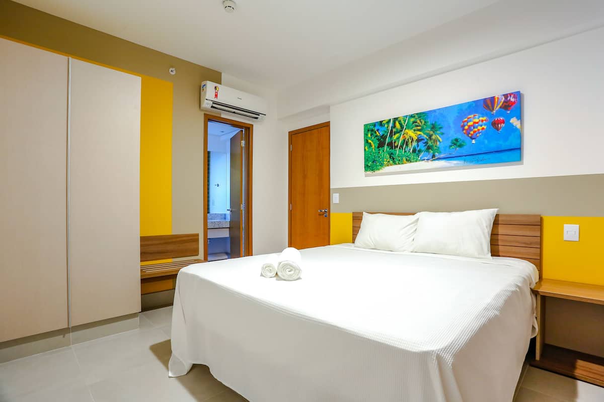A hotel room with a bed, a painting, a wardrobe, and an air conditioning unit.