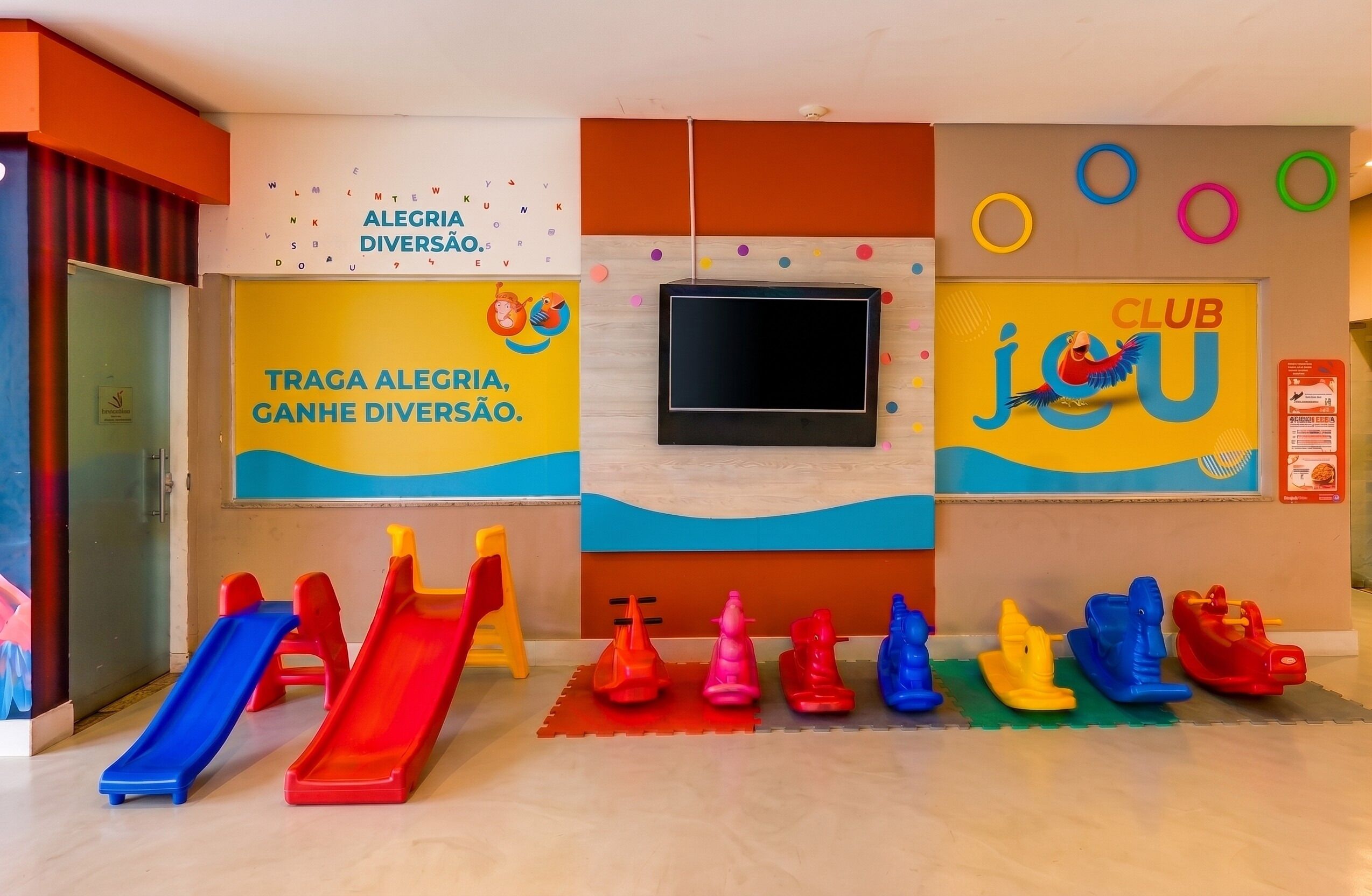 A children's play area with slides, rocking horses, and a TV screen.