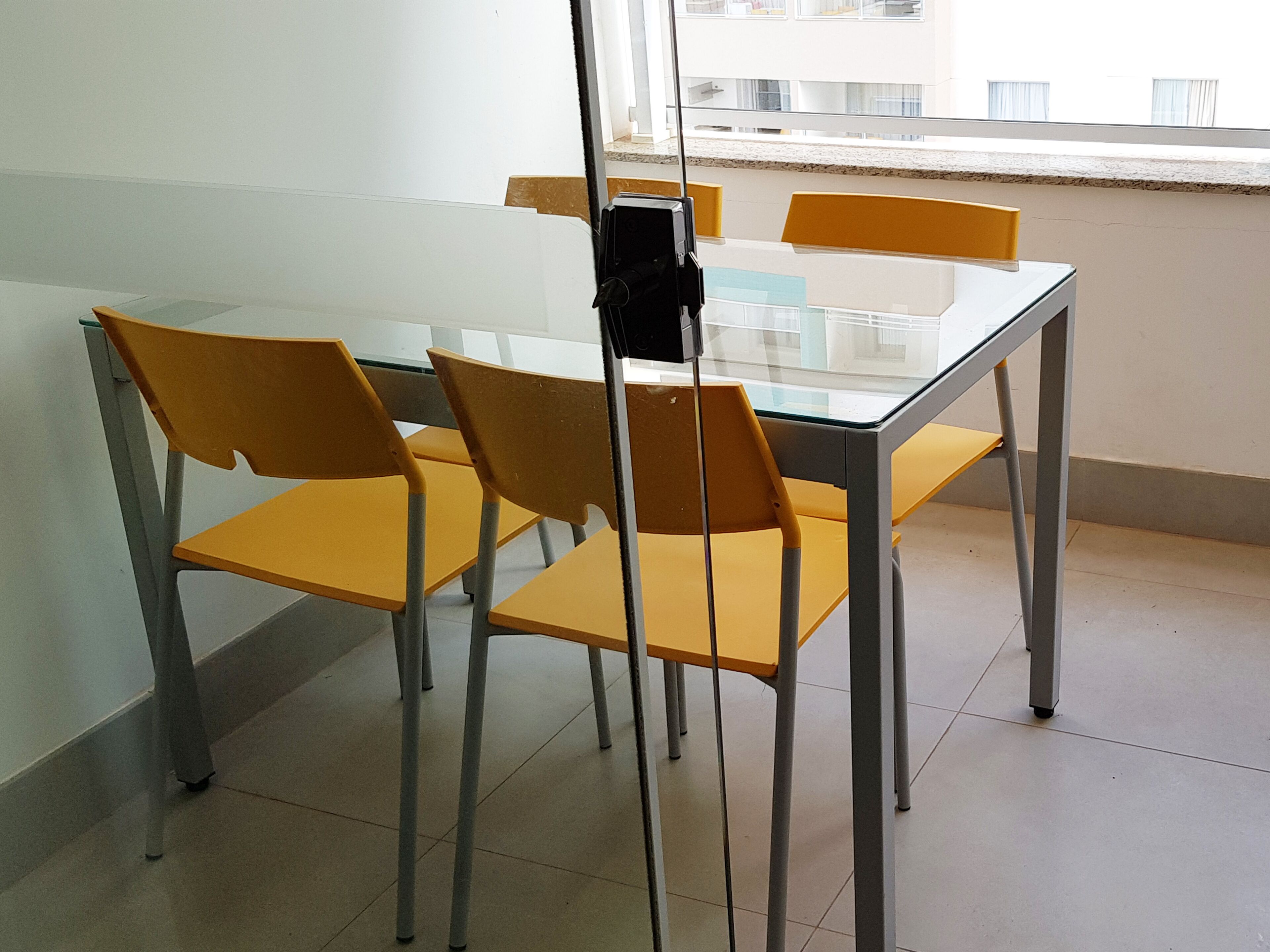 A room with a glass-top table and four yellow chairs.