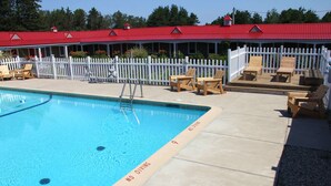 A swimming pool with a 'NO DIVING' sign, wooden deck chairs, and a white picket fence. - Mackinac Lake Trail Motel (Mackinaw City)