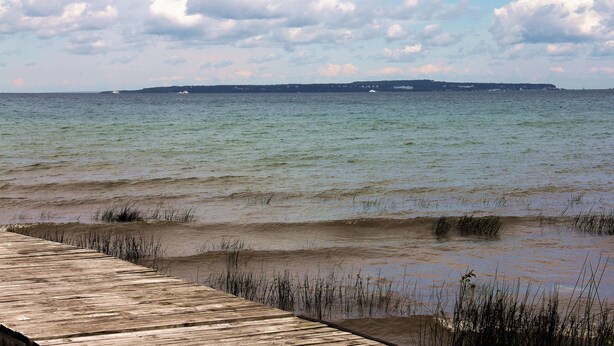 A wooden pier extending into calm waters with a distant shoreline and overcast sky. - Mackinac Lake Trail Motel (Mackinaw City)
