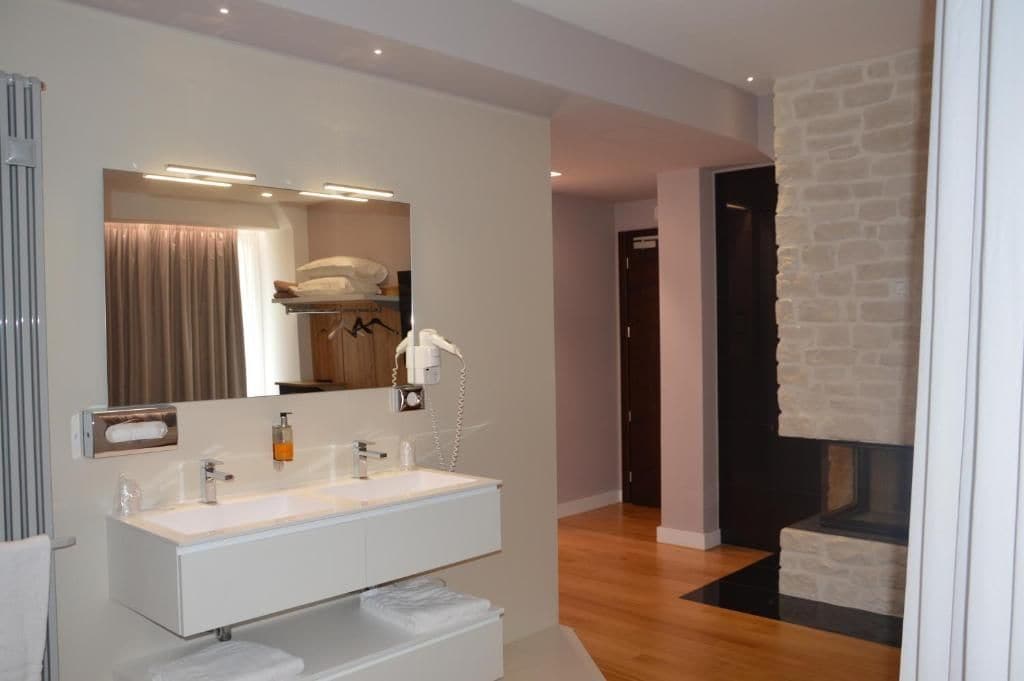 Une salle de bain moderne avec un grand miroir, un meuble-lavabo blanc et une cheminée en pierre.