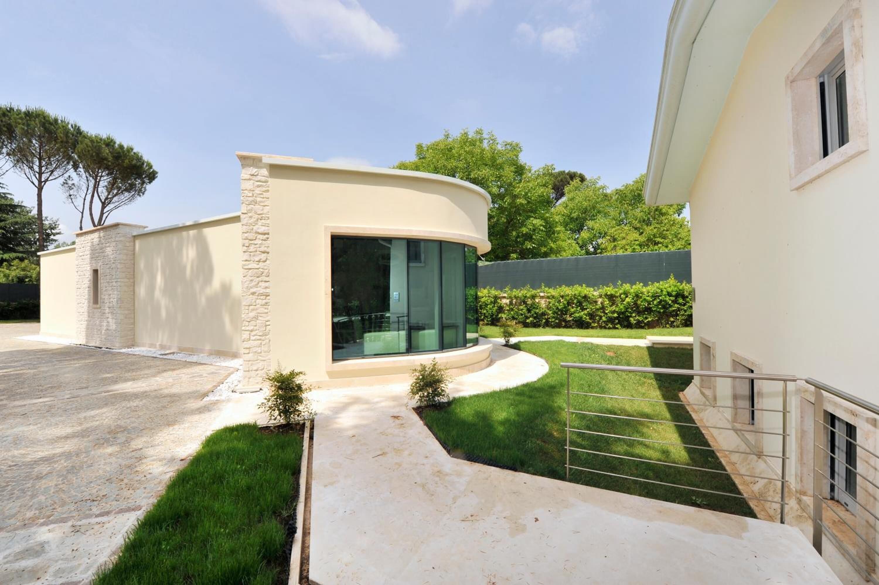 A modern house with a curved facade, a stone accent wall, and a glass door leading to a covered patio.