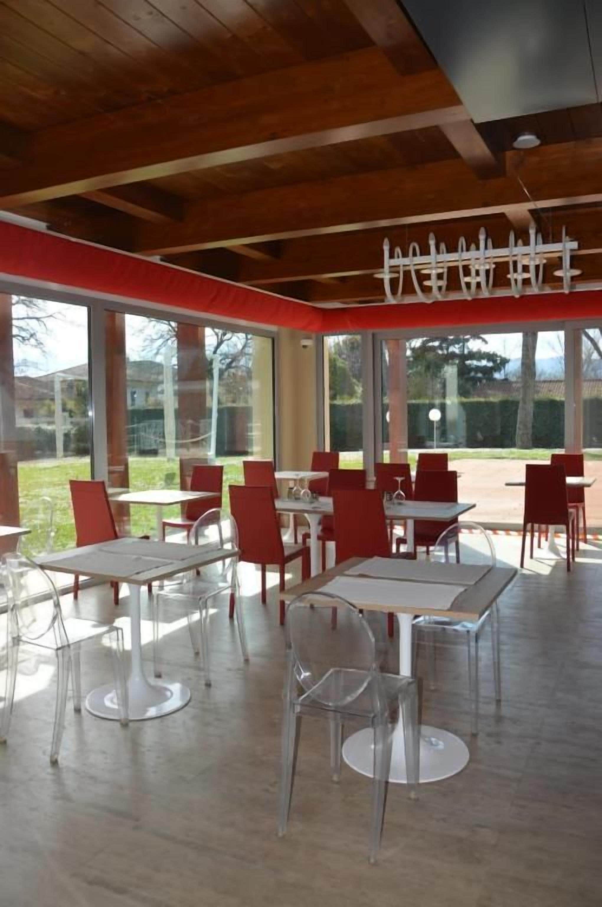 An indoor dining area with tables and chairs, large windows, and a wooden ceiling.
