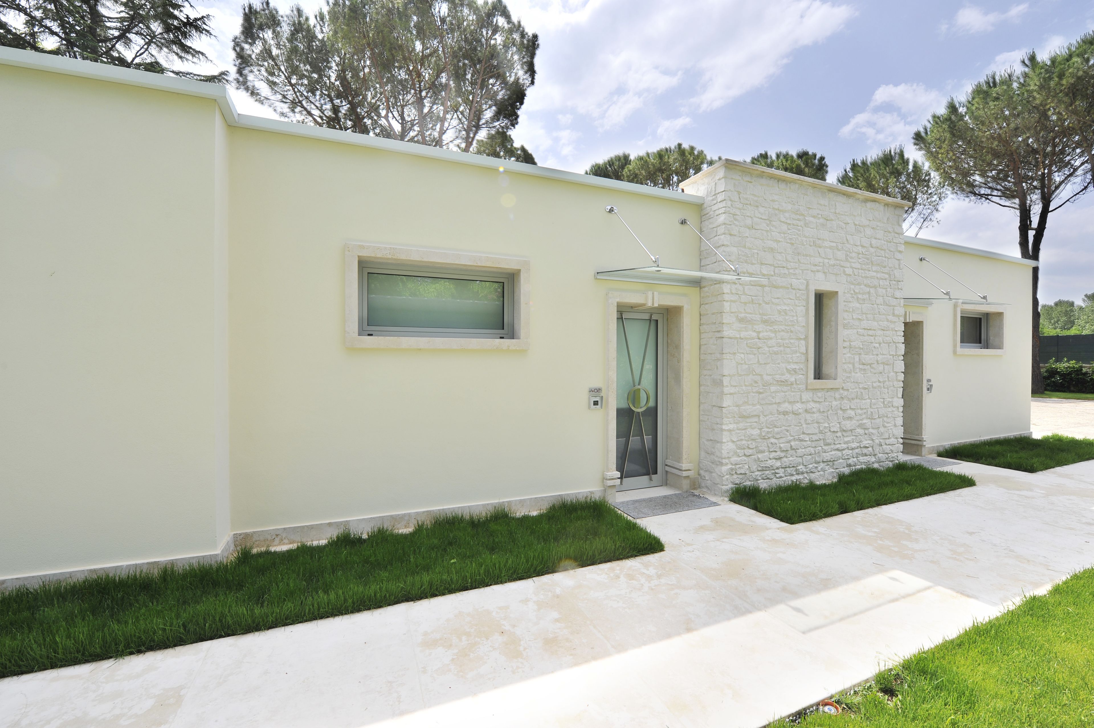 Una casa moderna con fachada clara, un muro de piedra decorativo y un pequeño jardín frontal con césped.