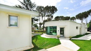Una casa moderna de dos pisos con fachada de vidrio curvo, un pequeño porche delantero y un césped bien cuidado.