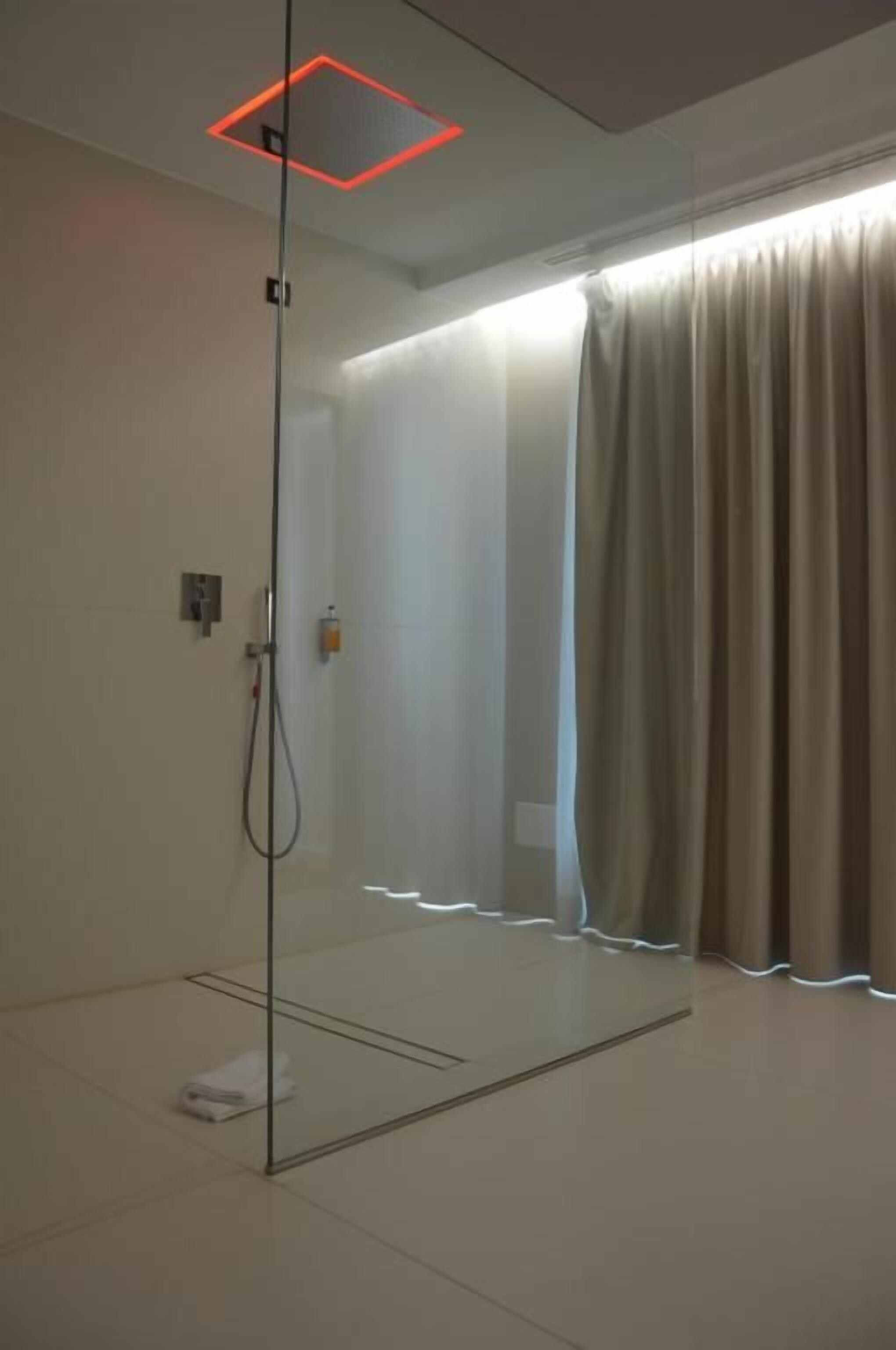 Una ducha con cerramiento de vidrio, un panel de control, un perchero y una cortina.