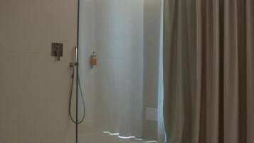 Una ducha con cerramiento de vidrio, un panel de control, un perchero y una cortina.