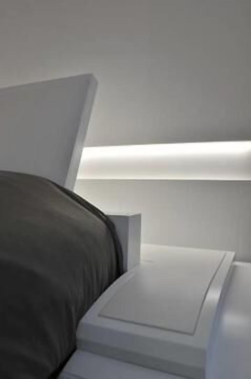 Un llit modern amb un panell frontal blanc i una taula de nit.