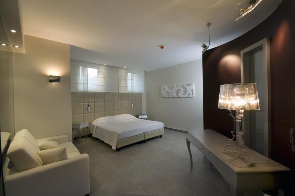 A modern hotel room with a bed, a sofa, a desk, and a lamp.