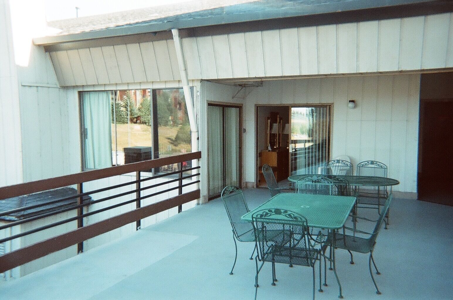A covered outdoor patio with a table and chairs, a railing, and a view of the surrounding area.