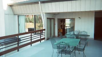 A covered outdoor patio with a table and chairs, a railing, and a view of the surrounding area.