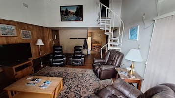 A living room with a TV, leather chairs, a sofa, a coffee table, and a staircase.