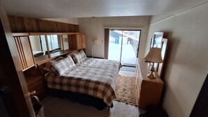A bedroom with a bed, wooden wardrobe, a nightstand, a lamp, and a view through a door. - Gondola Square, only 60 feet to the gondola. Best location. (Steamboat Springs)