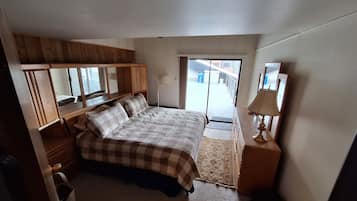 A bedroom with a bed, wooden wardrobe, a nightstand, a lamp, and a view through a door.