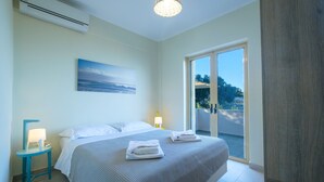Un dormitorio con cama, una mesita de noche, una lámpara, un cuadro y un ventanal corredero a un balcón.