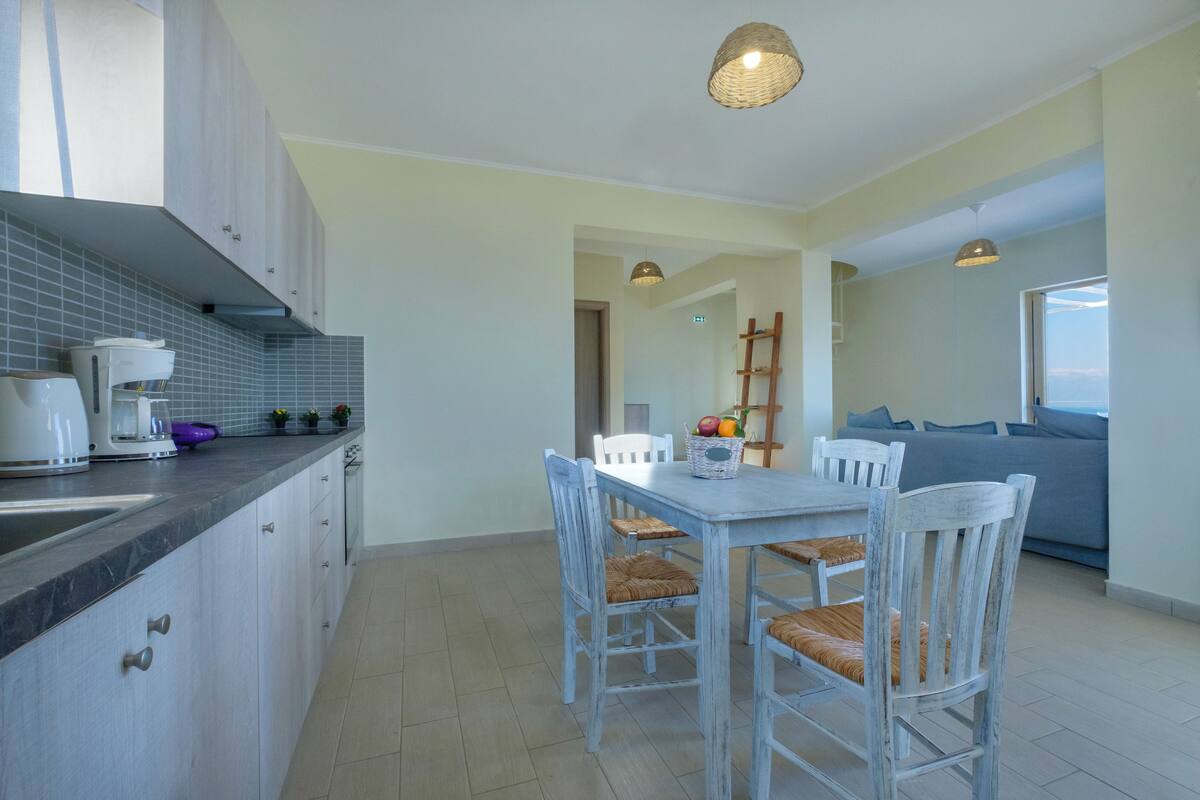 Una cocina moderna con comedor, que incluye una mesa, sillas, una cafetera y una cesta de frutas.