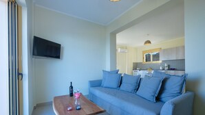 Una sala de estar con un sofá, una mesa de centro con una botella y vasos, y un televisor montado en la pared.
