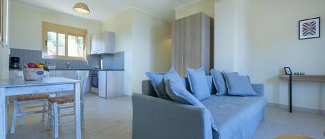 A modern living room with a blue sofa, a dining table with chairs, and a kitchen area with a window.